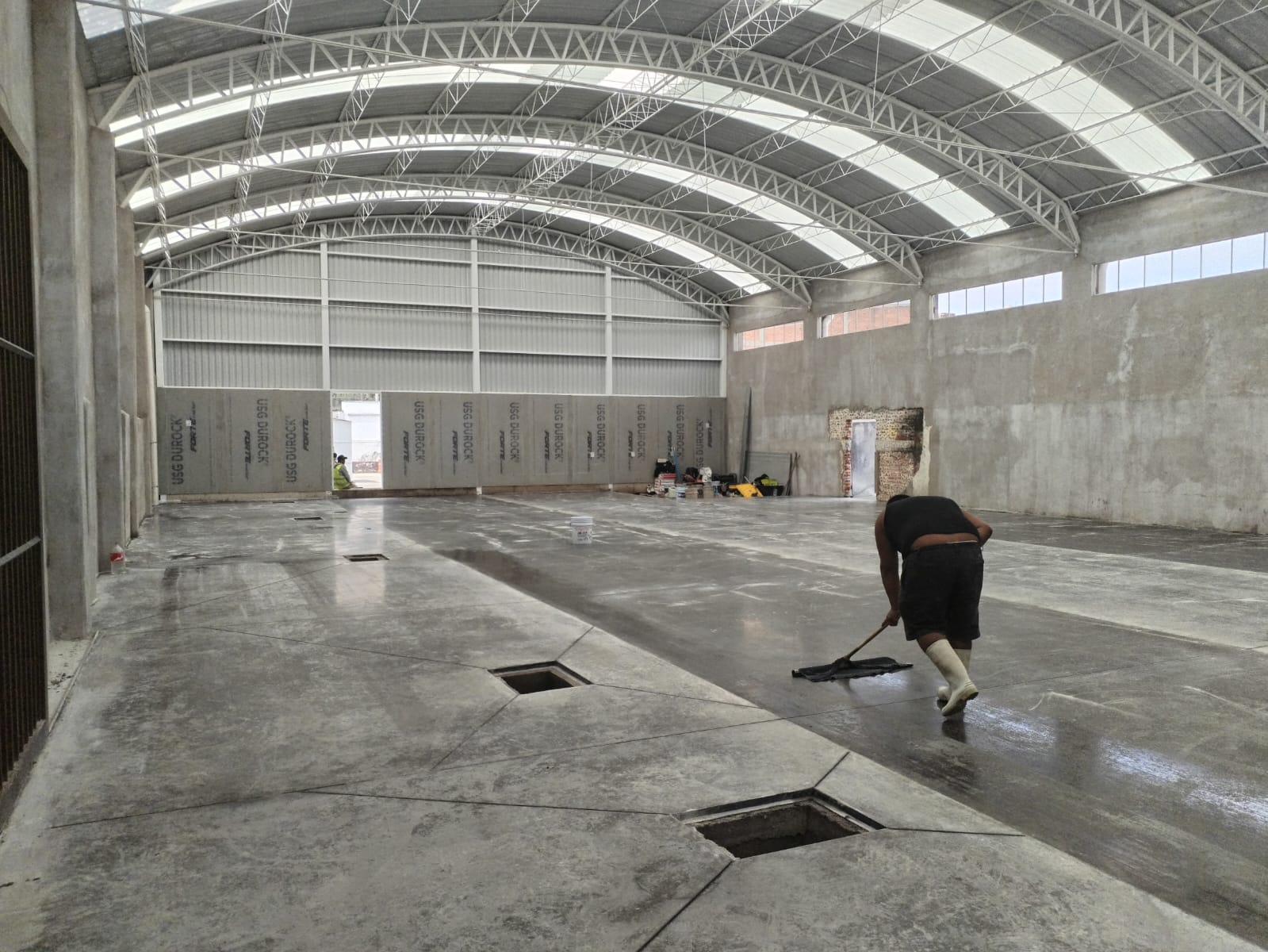 Vista interior de una construcción con estructura metálica y trabajos en el piso